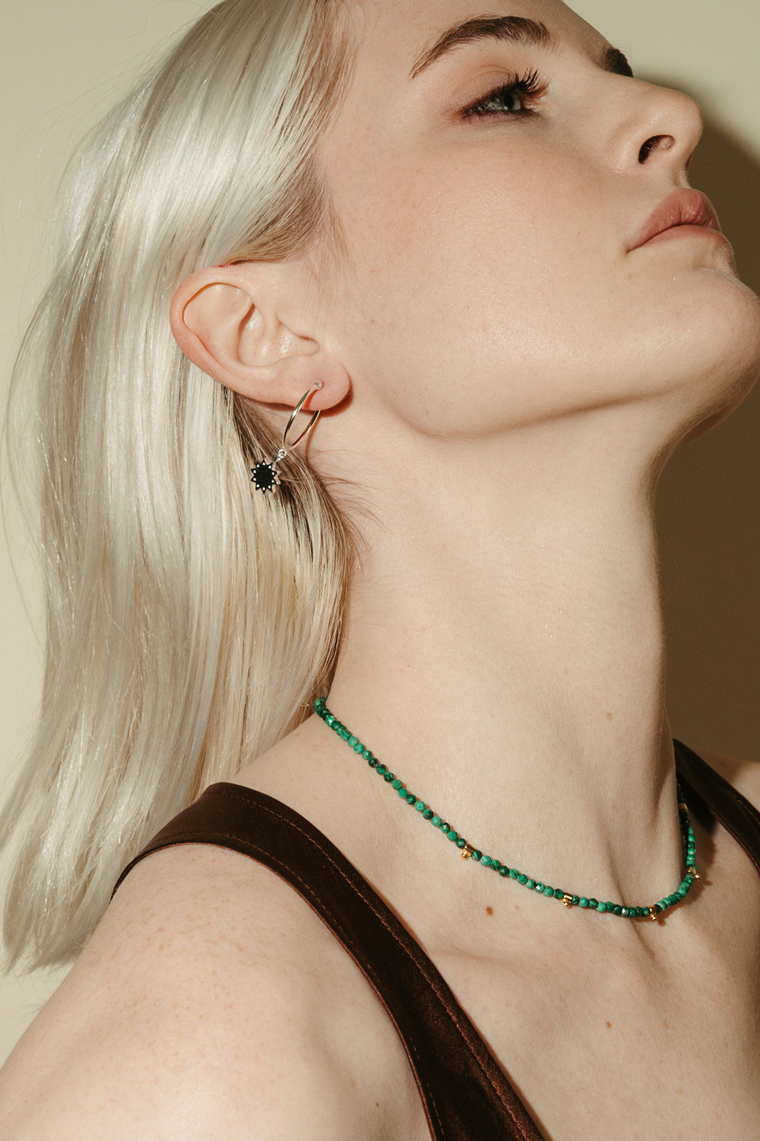 Woman wearing a green malachite beaded necklace and hoop earrings against a neutral background