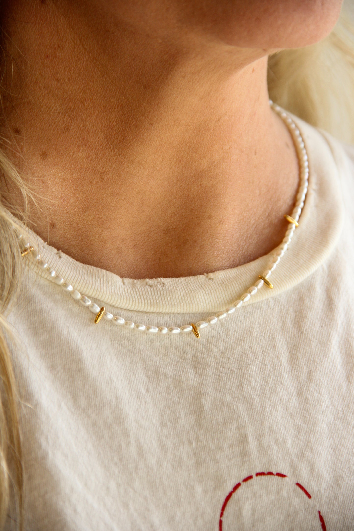 Close-up of a person wearing a small pearl necklace with gold accents