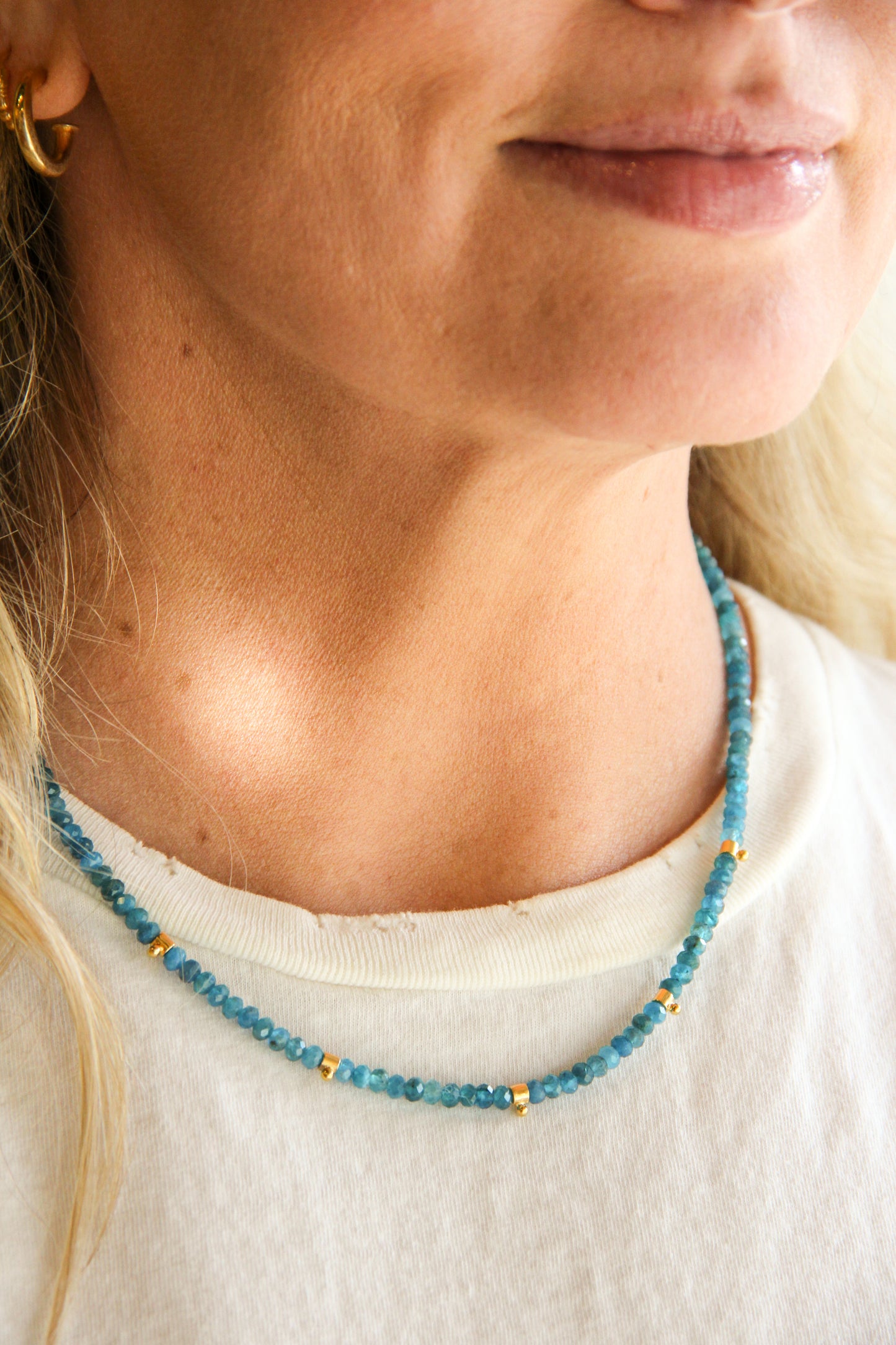 Close-up of a person wearing a blue beaded necklace with a neutral background