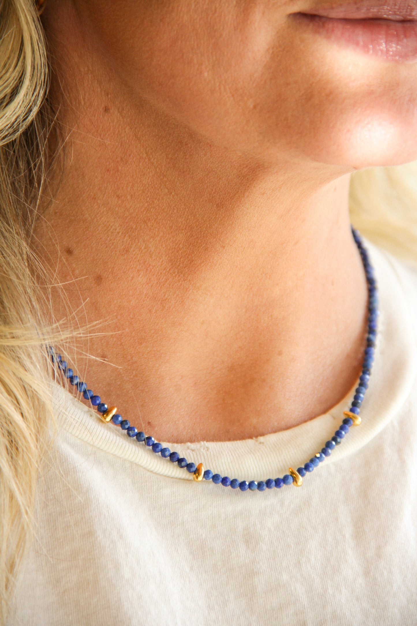 Close-up of a person wearing a blue beaded necklace with gold accents