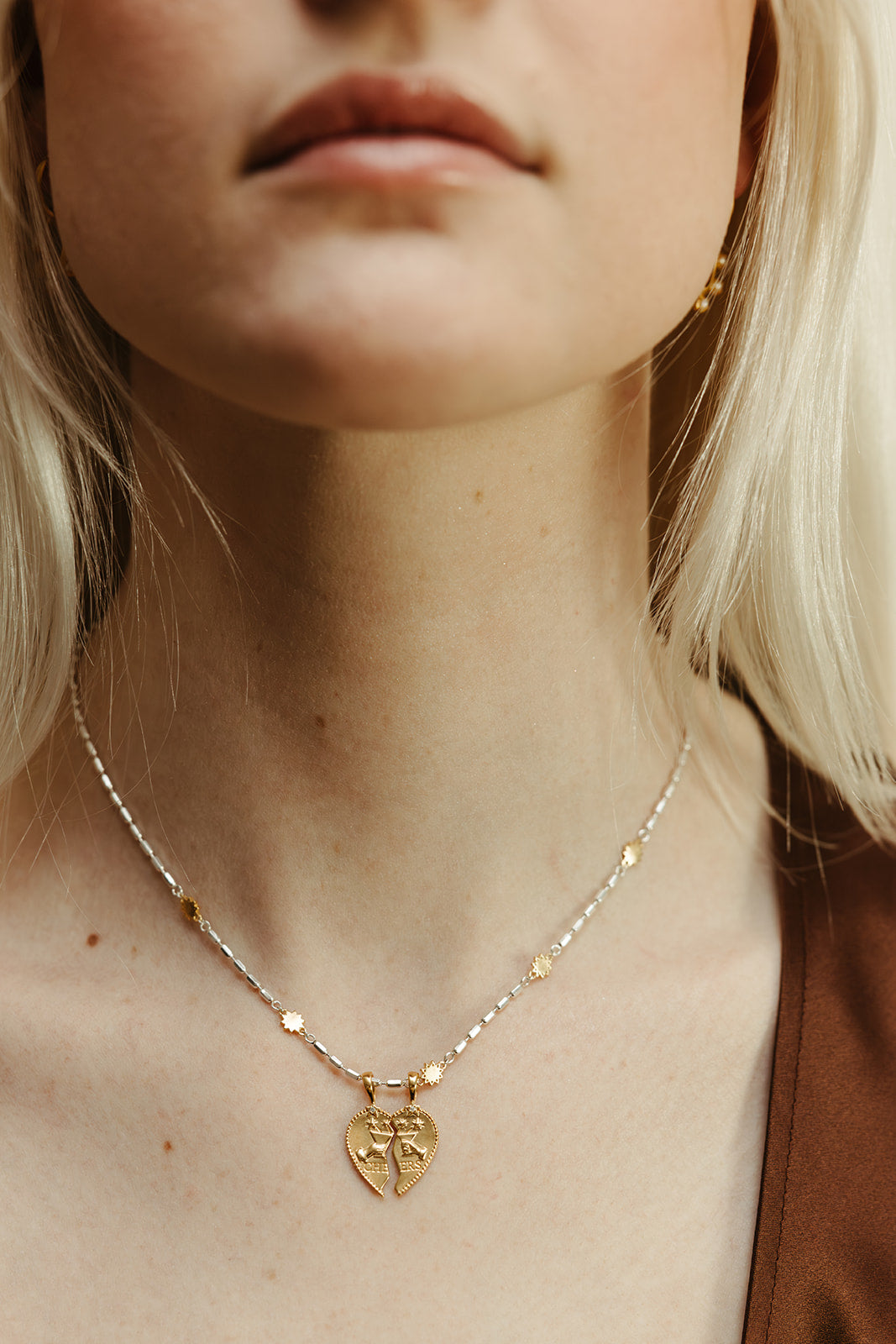 Close-up of a person wearing a gold necklace with a heart-shaped pendant.