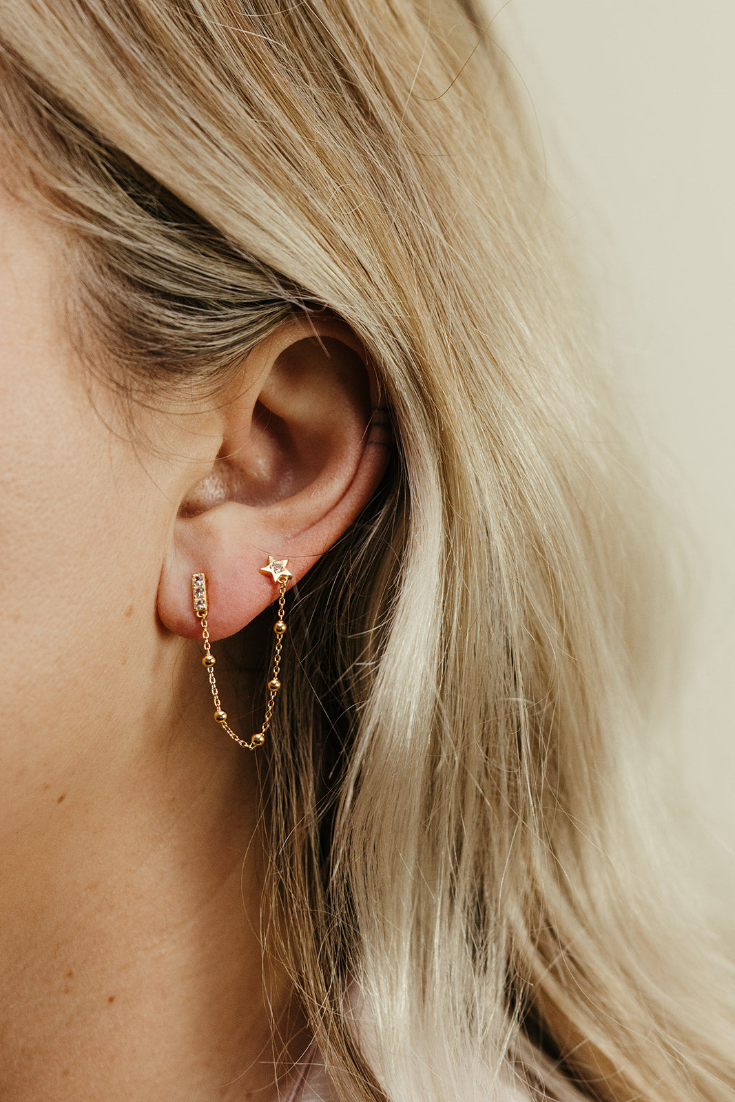 Close-up of a person wearing gold connected stud earrings with star details.